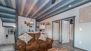Een woonkamer met een bruine bank, een ronde salontafel en een eethoek met een witte kast en een kroonluchter.