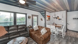 Een moderne woonkamer met een bruine leren bank, een houten salontafel en een eethoek met een witte tafel en stoelen.