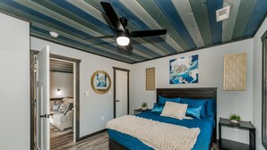 Een slaapkamer met een groot bed, een plafondventilator en uitzicht op een andere kamer.