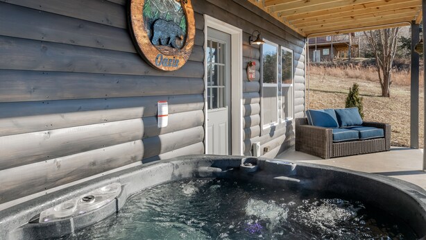 Een houten chalet met een jacuzzi, een bord waarop staat 'Shaconage Oasis' en een rieten bank buiten.