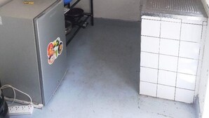 Een kleine keuken met een koelkast, een spoelbak en een plank boven het aanrecht.
