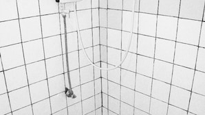 Een kleine douchecel met betegelde wanden, een handdouche en een zeepdispenser.