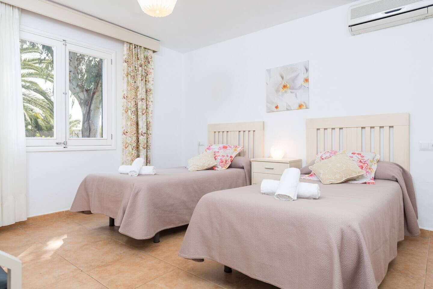 A hotel room with two beds, a window with curtains, a ceiling light, and a wall-mounted air conditioner.
