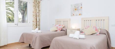 A hotel room with two beds, a window with curtains, a ceiling light, and a wall-mounted air conditioner.