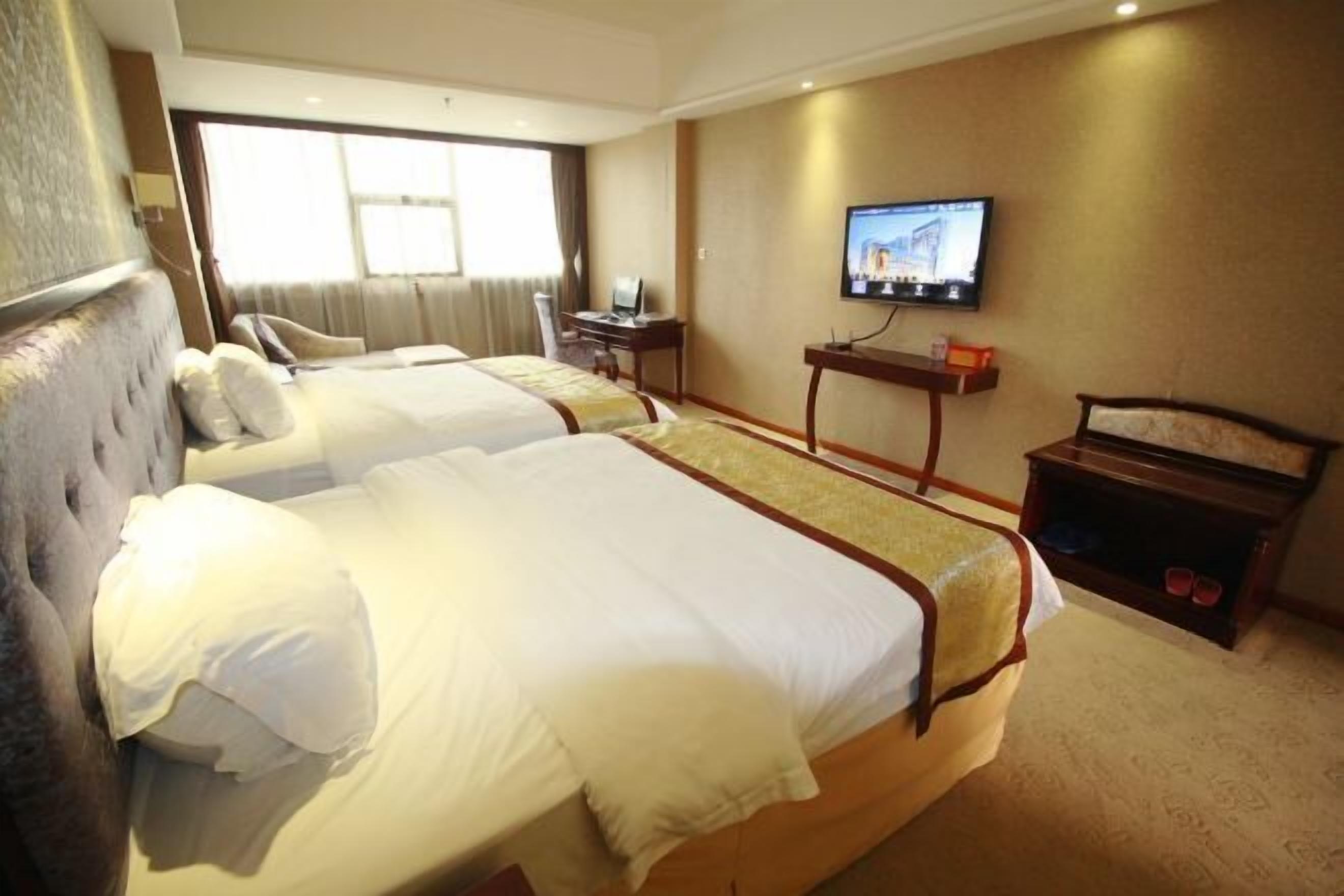 A hotel room with two beds, a television on the wall, and a desk with a chair.