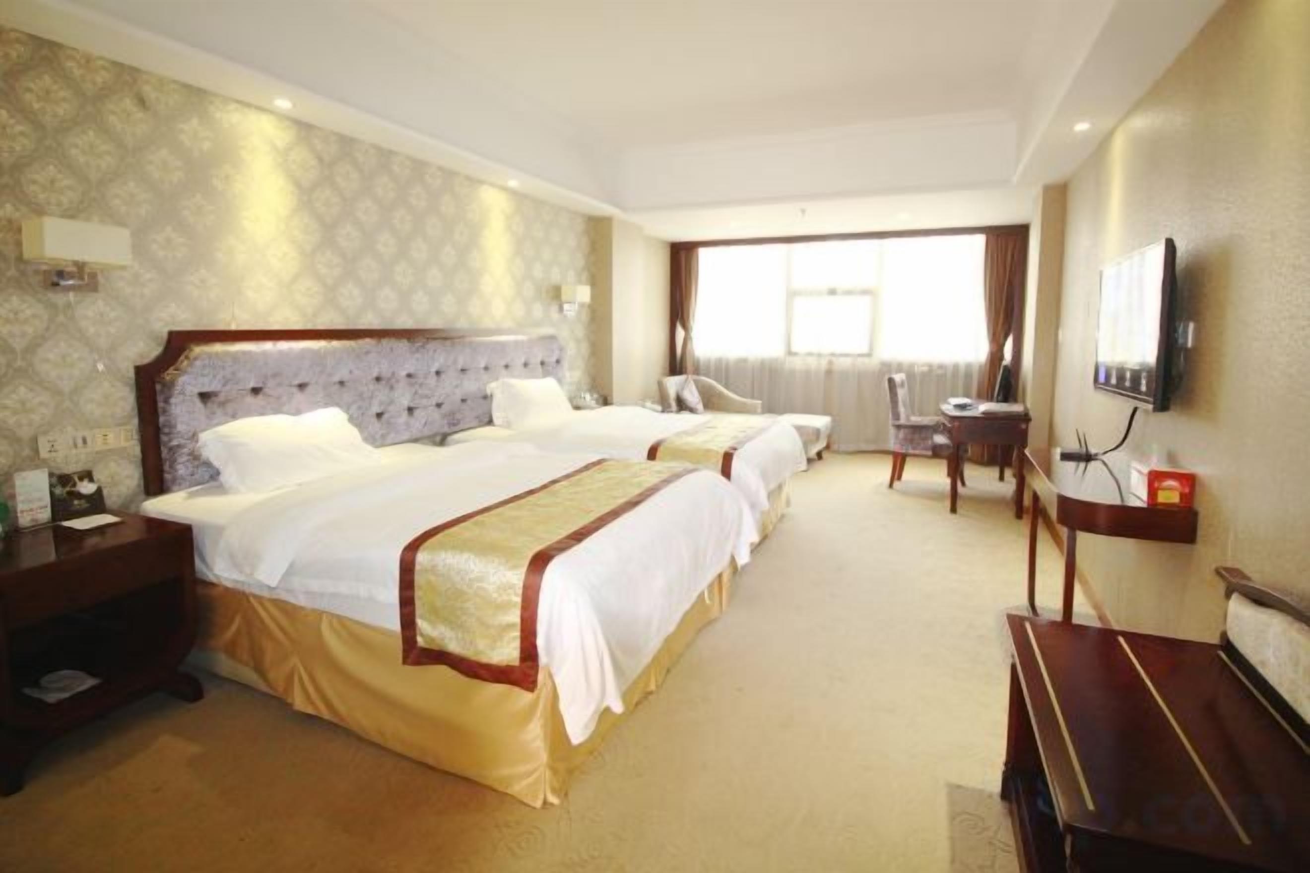 A hotel room with two beds, a desk, a chair, and a television.