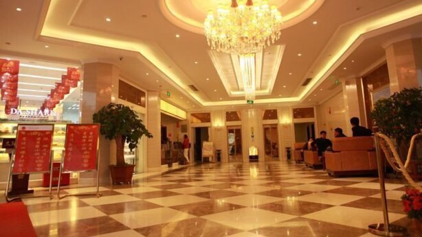 Un vestíbulo de hotel con piso a cuadros, un candelabro y una zona de recepción con asientos.