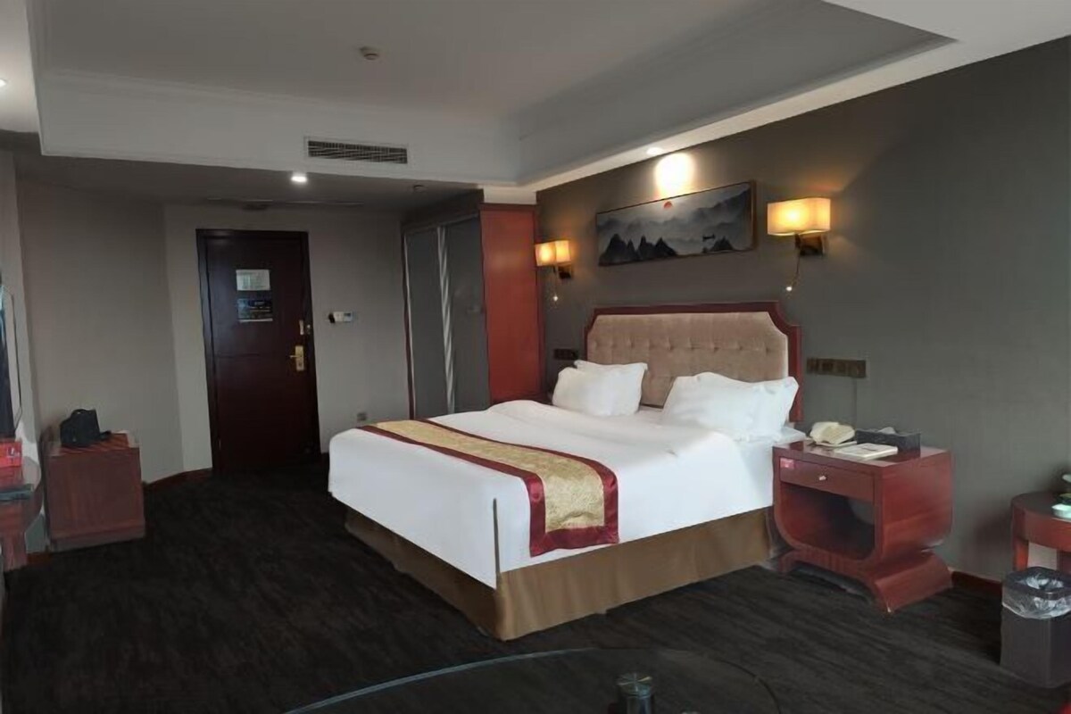 A hotel room with a large bed, a nightstand, a wall-mounted lamp, and a door.