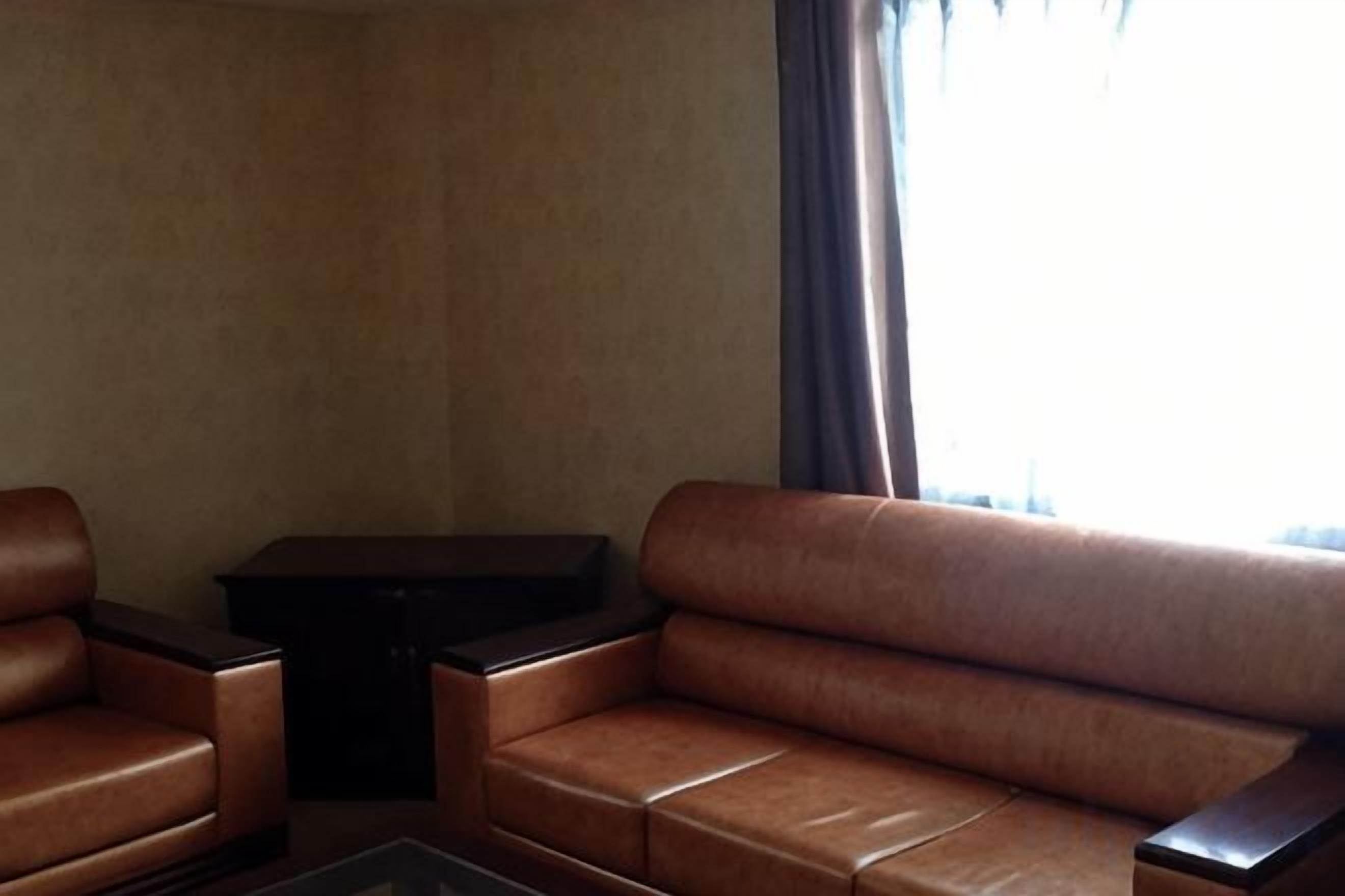 Una habitació amb un sofà de cuir marró, una taula auxiliar petita negra i una finestra amb cortines.