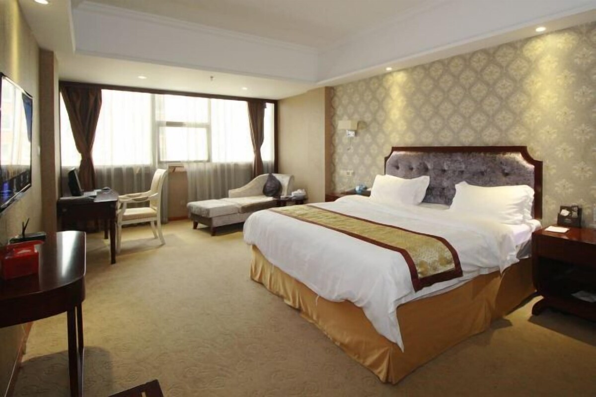 A hotel room with a large bed, a desk, a chair, and a TV.