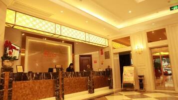 A hotel reception area with a checkered floor, a reception desk, and a glass door entrance.
