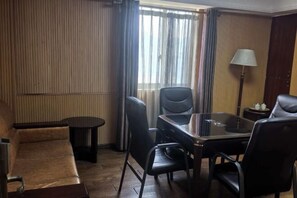 Et hotelværelse med sofa, et bord med glasplade og stole, en lampe og et vindue med gardiner.
