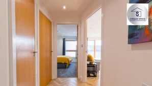 A hallway leading to a bedroom with a bed, a desk, and a chair.