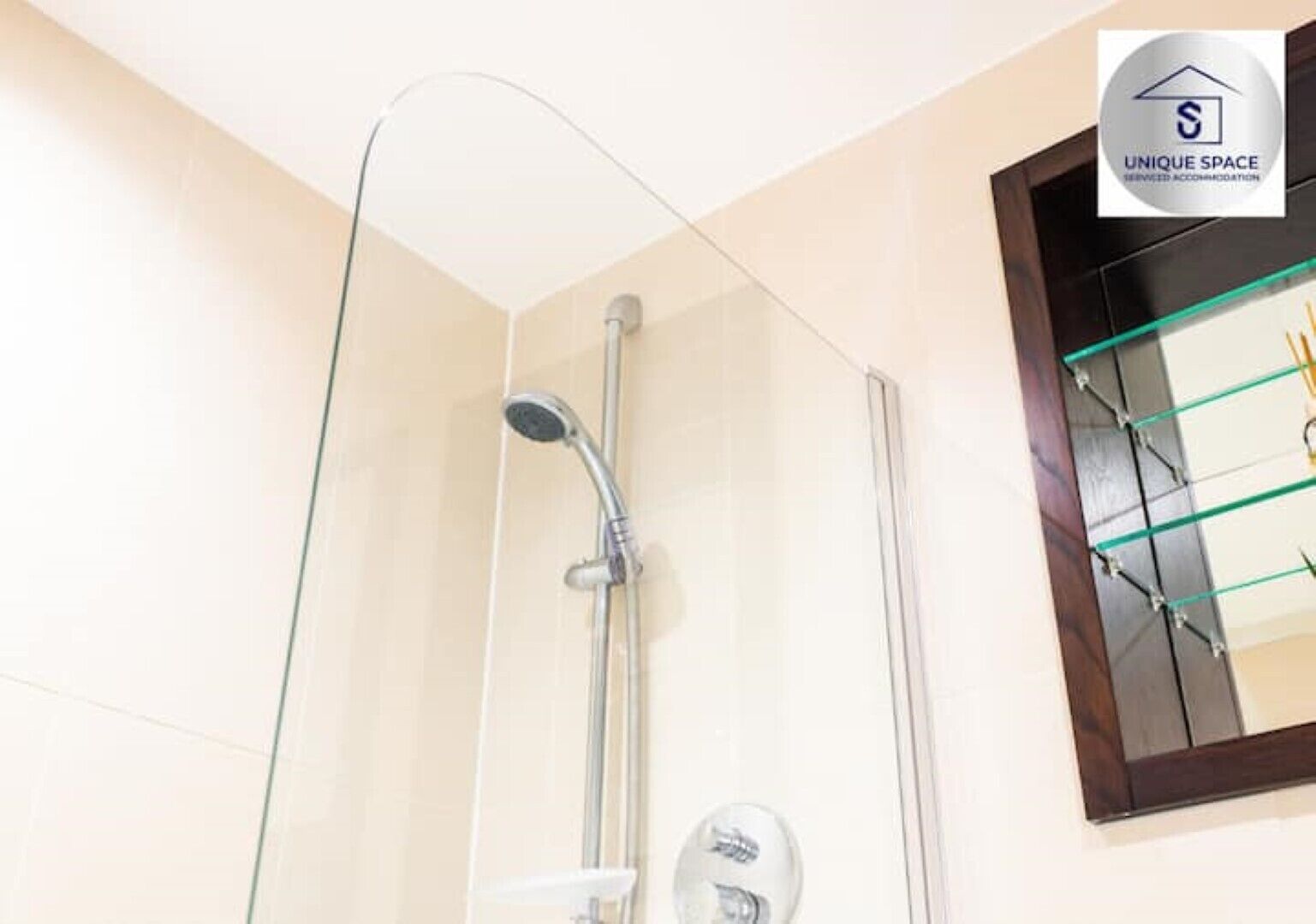 A modern bathroom with a glass shower enclosure, a wooden-framed mirror, and a towel rack.