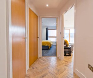A hallway leading to a bedroom with a bed, a desk, and a chair.
