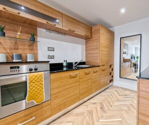 A modern kitchen with wooden cabinets, stainless steel appliances, and a herringbone floor pattern.
