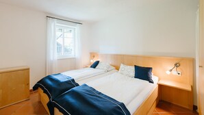 A double bed with a wooden headboard, two bedside tables with lamps, a window with curtains, and a wooden cabinet. - Allgäu a. Forggensee - near Neuschwanstein, apartment f. Couples and family, 2 bedrooms, WLAN (Roßhaupten)