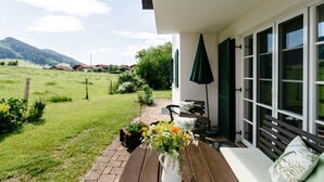 A patio with a wooden table, a white vase with flowers, and a bench. - Allgäu a. Forggensee - near Neuschwanstein, apartment f. Couples and family, 2 bedrooms, WLAN (Roßhaupten)