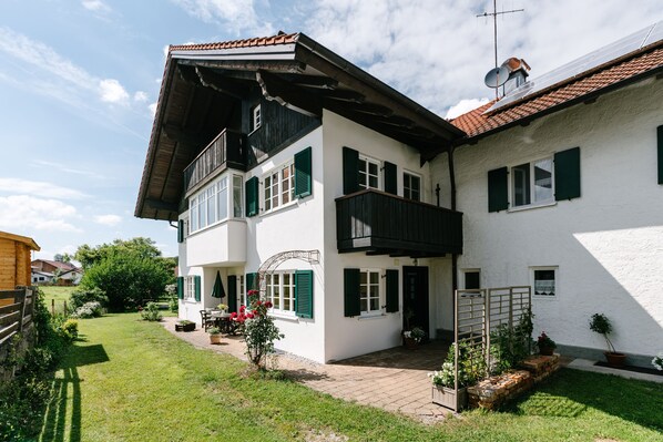 A two-story house with a balcony, a garden, and a brick pathway.