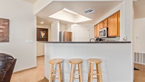 Una cocina moderna con una isla central, taburetes de madera y un comedor con una silla de cuero marrón.