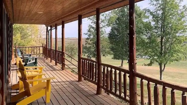 A wooden deck with a railing, a table, and yellow chairs.