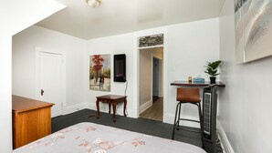 Une chambre à coucher comprenant un lit, un bureau, une chaise, un radiateur, une porte et un couloir menant à une autre pièce.