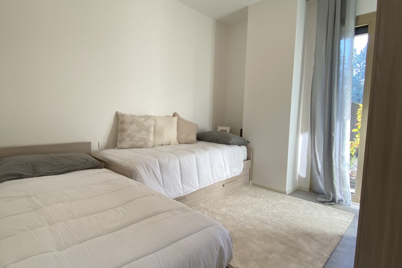 A bedroom with two beds, a carpeted floor, and a view of the outdoors through a window with curtains.