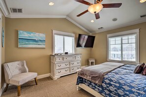 A bedroom with a bed, a dresser, a chair, a ceiling fan, and a TV on the wall.