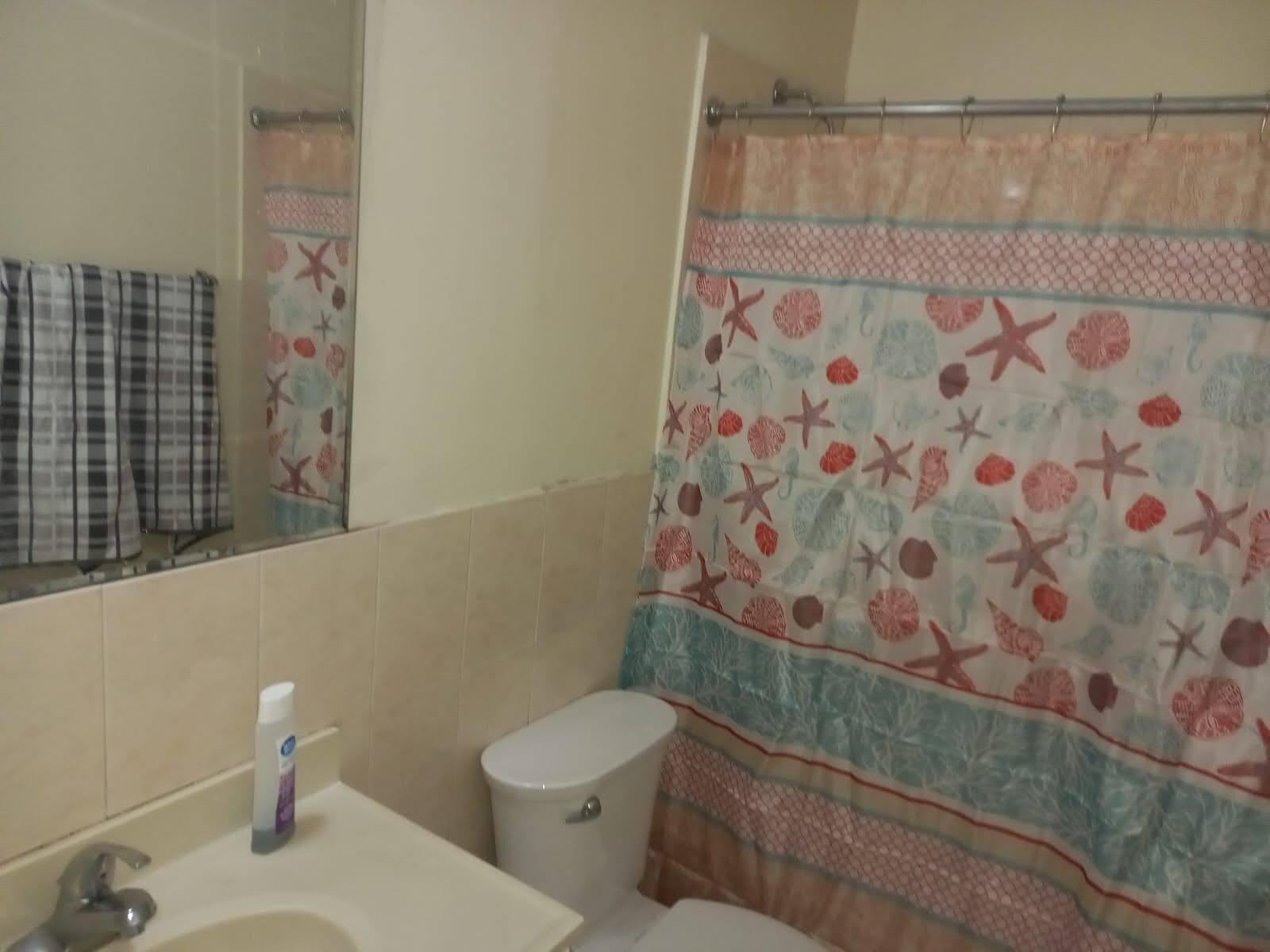 Un baño con inodoro, lavabo y cortina de ducha con diseño de estrellas de mar y conchas.