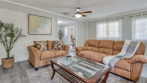 Ein Wohnzimmer mit zwei braunen Sofas, einem Glastisch, einem Deckenventilator und einer großen Weltkarte an der Wand.