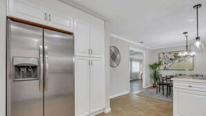 Eine moderne Küche mit weißen Schränken, einem Edelstahl-Kühlschrank und einem Essbereich mit einer Pendelleuchte.