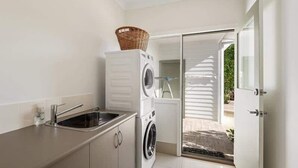 A laundry area with a washing machine, a sink, and a basket on a cabinet. - Casa Bianca—Oceanview Beachside Escape (Dunsborough)