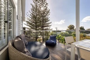 A balcony with wicker furniture, a glass railing, and a view of trees and a distant landscape.