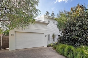 A residential garage with a white exterior, a driveway, and surrounding vegetation.