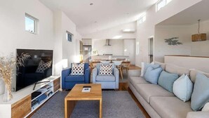 A modern living room with a TV, sofas, a coffee table, and a kitchen in the background. - Casa Bianca—Oceanview Beachside Escape (Dunsborough)
