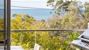 A balcony with a table and chairs, overlooking a natural landscape with trees and a view of the sea. - Casa Bianca—Oceanview Beachside Escape (Dunsborough)