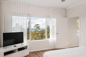 A bedroom with a TV, a bed, a window with curtains, and a door.