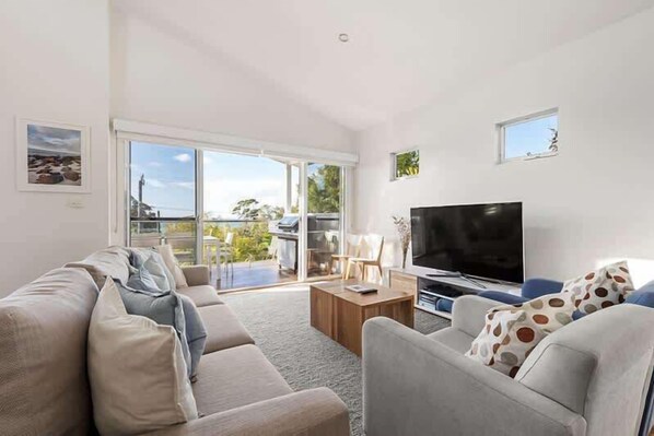 A spacious living room with a large TV, a sofa, a coffee table, and a view through the glass doors.