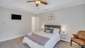 Een slaapkamer met een bed, een plafondventilator, een televisie, een nachtkastje en een lederen fauteuil.