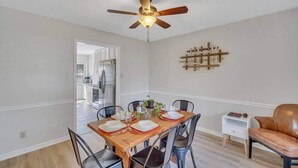 Een eethoek met een houten tafel voor vier personen, omringd door stoelen, een plafondventilator en een wandlamp.
