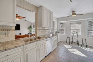 A kitchen with white cabinets, a granite countertop, a dishwasher, and a ceiling fan.