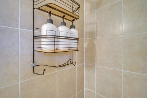 A bathroom with a tiled wall and a metal shelf holding three bottles.