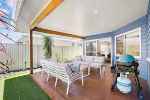 Une terrasse extérieure avec une plateforme en bois, des meubles blancs et un barbecue au propane.