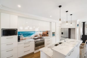 Une cuisine moderne avec des meubles blancs, un îlot central, un four à micro-ondes, un four et des luminaires suspendus.