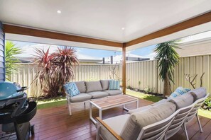 Un patio techado al aire libre con una parrilla, una mesa de madera y dos sofás con cojines.