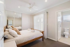 A bedroom with a bed, a ceiling fan, a window with curtains, and a bathroom with a toilet.