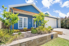 A residential house with a garage, a front yard with various plants, and a clear blue sky.