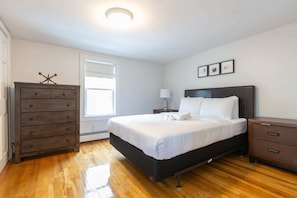 Un dormitorio con cama, cómoda, mesita de noche y ventana.