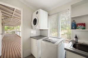 Eine kompakte Küche mit integrierter Waschmaschine und Trockner, einer kleinen Arbeitsfläche und einem Fenster mit Jalousien.
