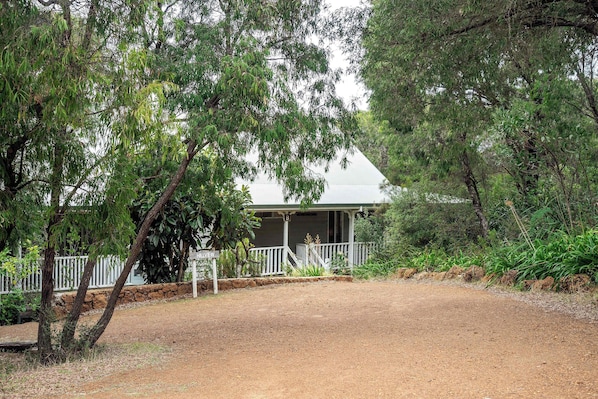 A building with a porch, surrounded by trees and a dirt path.